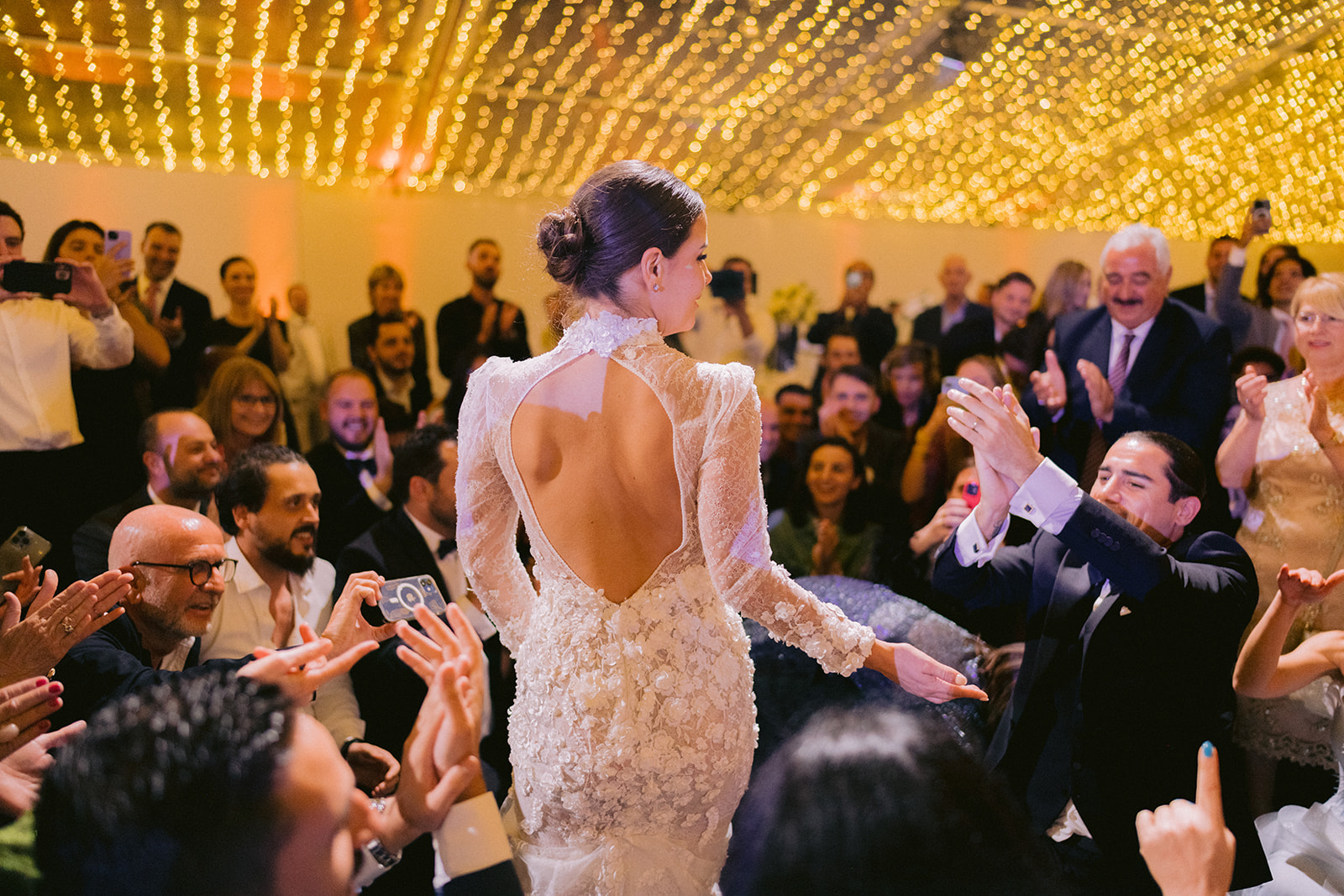 la mariée danse devant tous les invités qui l'applaudissent de joie en voyant son visage illuminé de toutes flamme sans oublier sa robe à dos nu